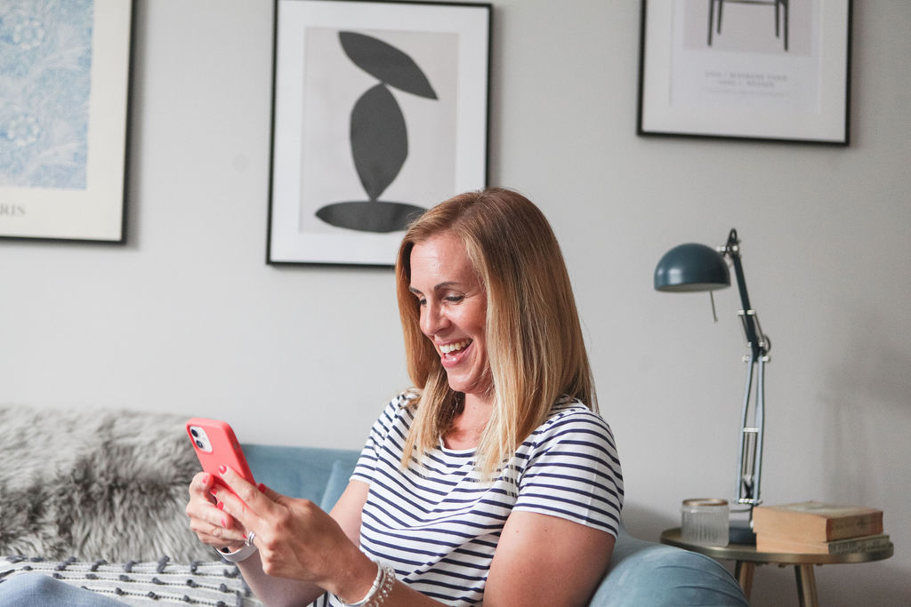 female business founder sat sideways on sofa smiling and working on her mobile phone